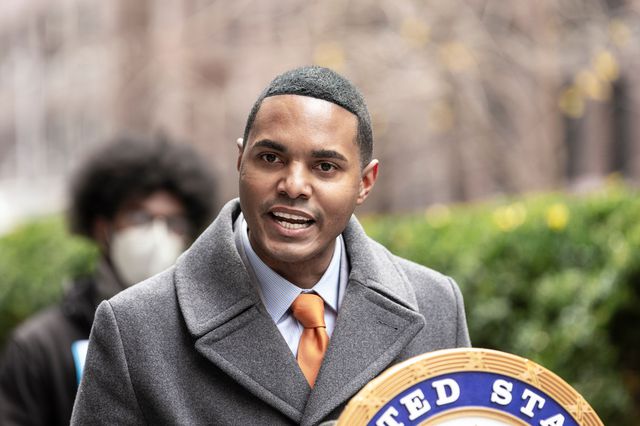 Ritchie Torres, wearing a coat over a suit, behind a lectern on a midtown Manhattan sidewalk